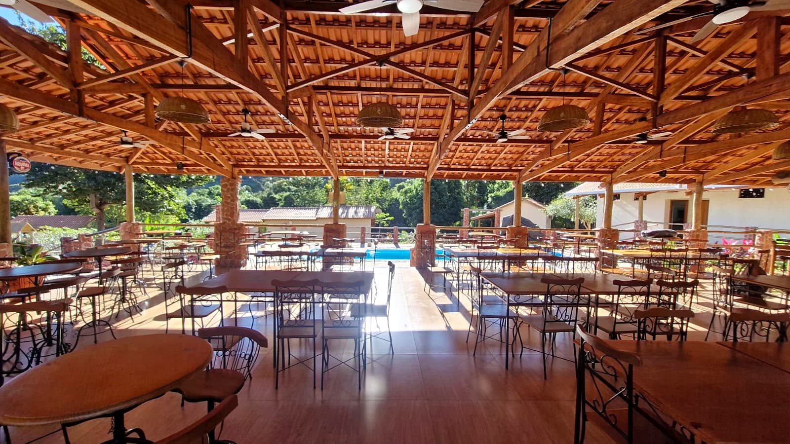 Inside the wooden pavilion with tables, woven lights, and a view of the pool.