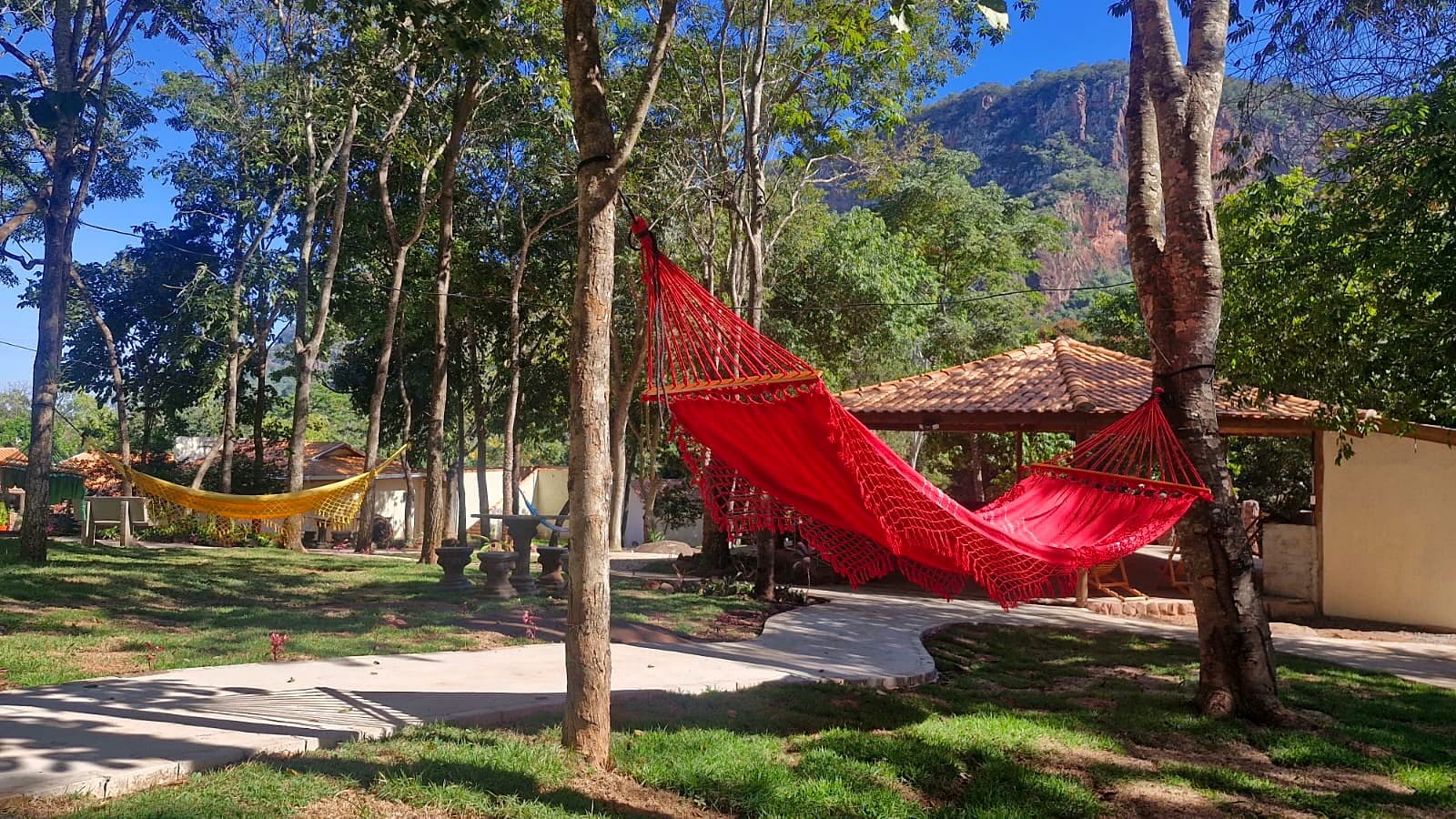 Red hammock on the shaded lawn, with a pavilion and the hills beyond.