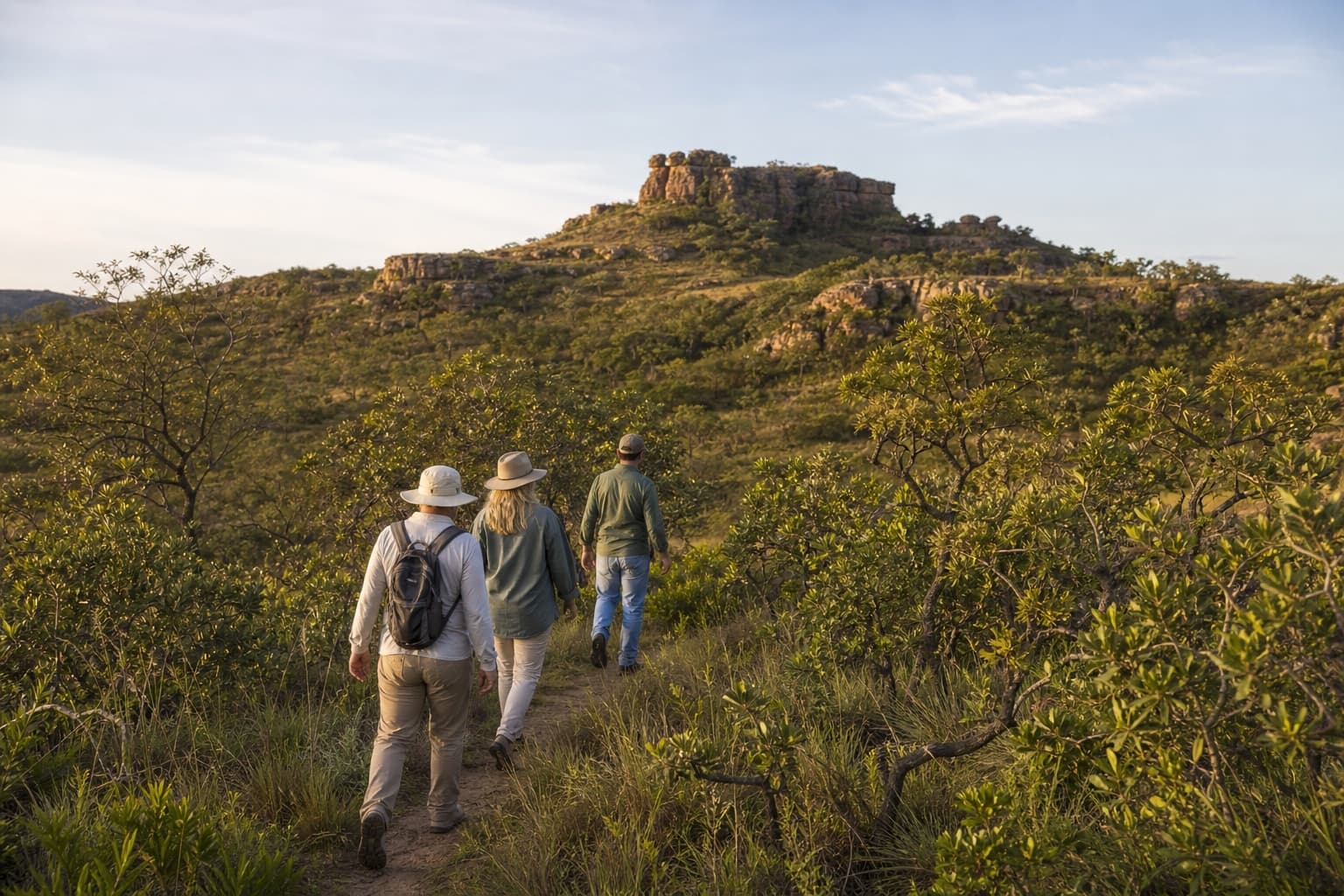 Guide leading two visitors on a trail through cerrado vegetation and rock formations.